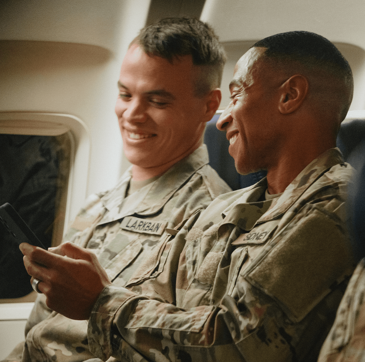 two soldiers talking and laughing together on an airplane
